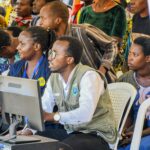 A diverse group of adults engaging with technology at a community event in Rwanda.