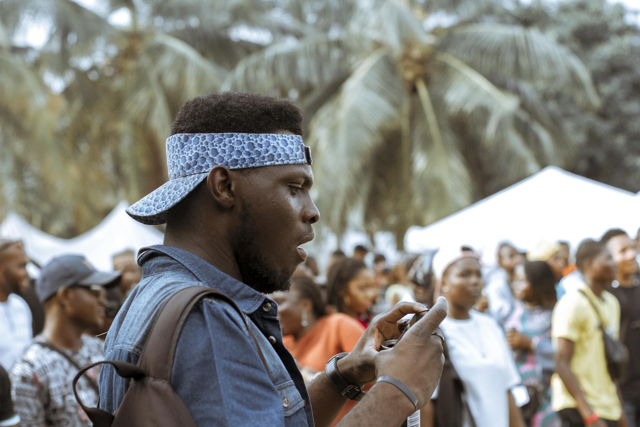 A young man in a vibrant street festival captures moments with his phone.