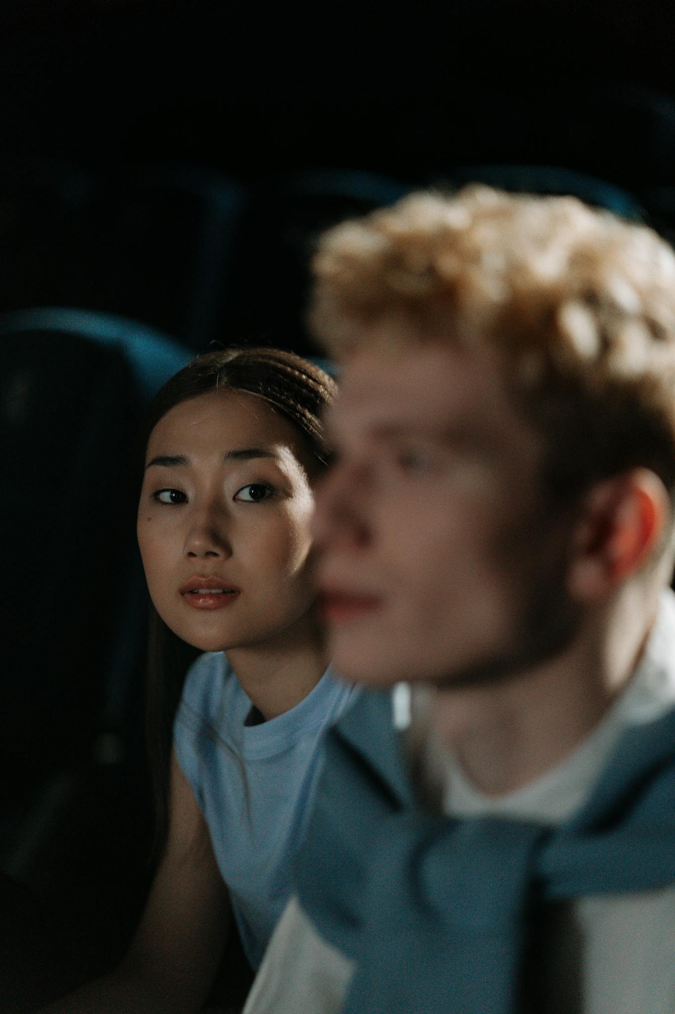 An Asian woman and a Caucasian man sitting in a cinema, enjoying a date night.