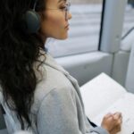 Side view of a woman with headphones writing in a notebook while sitting on a bus.